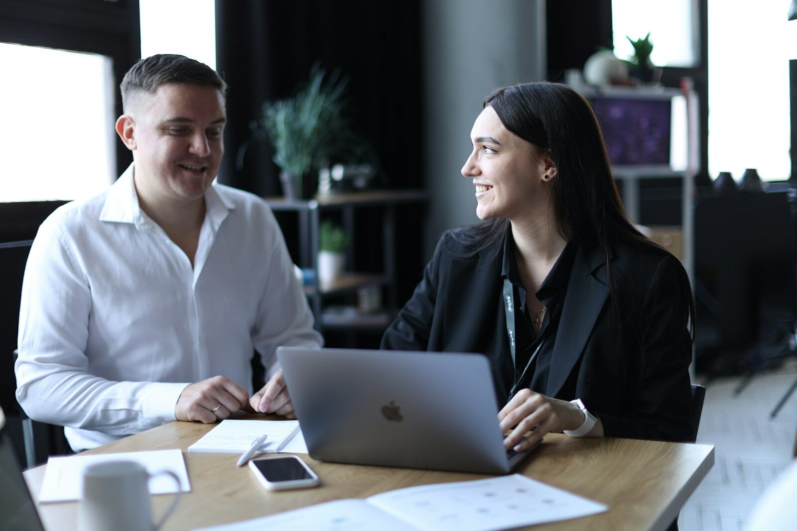 Professionals engaging in a discussion over a laptop at a modern workspace. The atmosphere is collaborative and friendly.