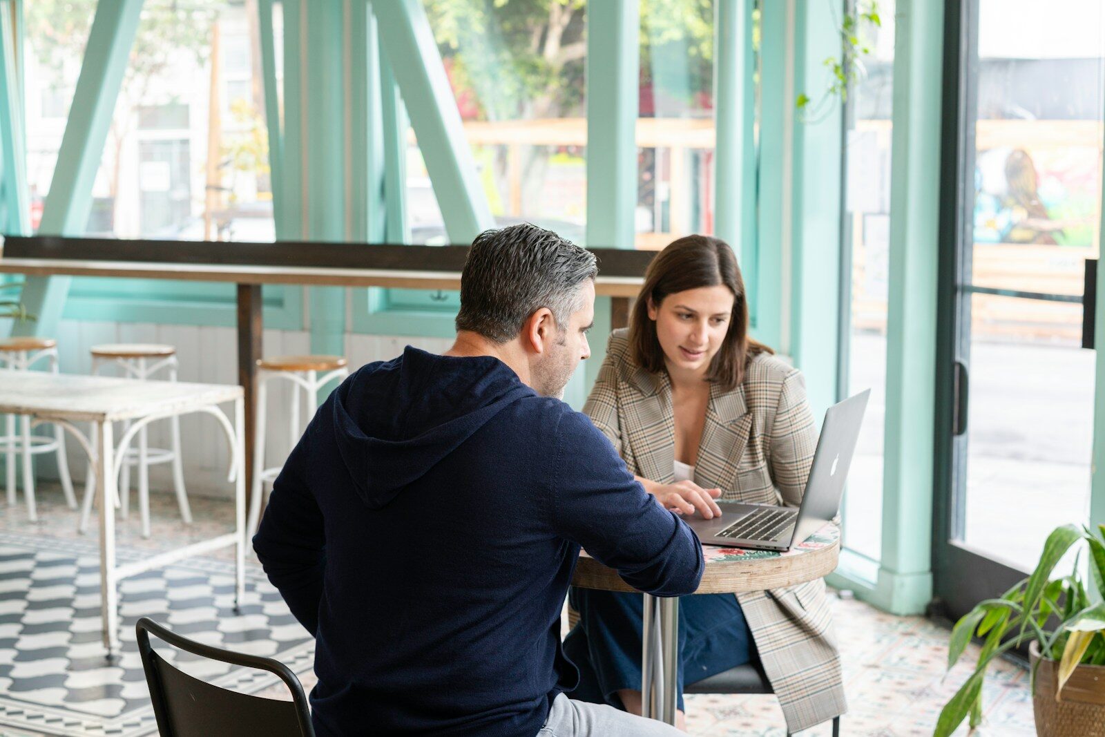 Two professionals collaborate at a table in a bright, modern café, focused on a laptop. Natural light enhances the inviting atmosphere.