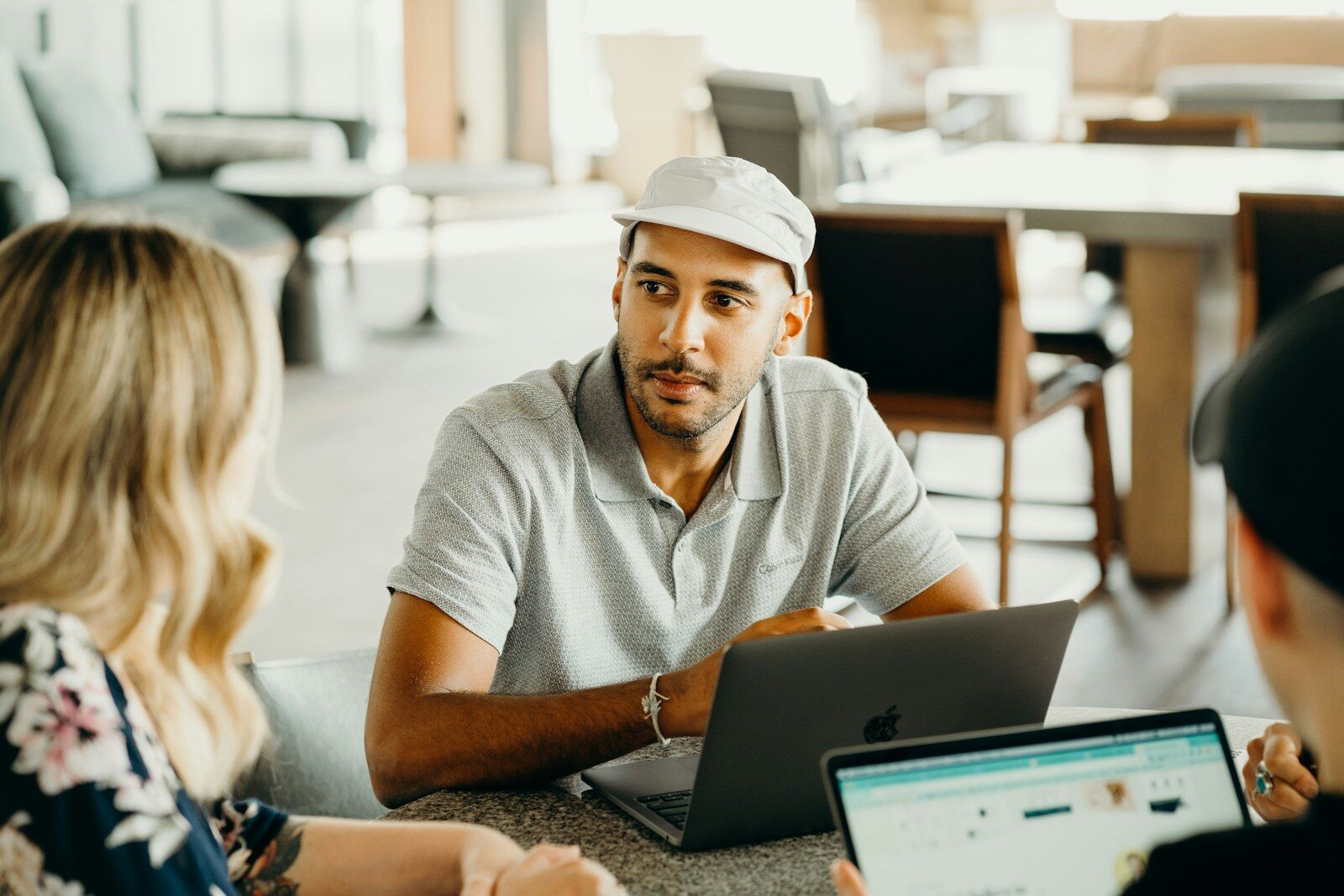 A man in a cap listens attentively during a discussion with two others at a modern workspace, highlighting collaboration and engagement.